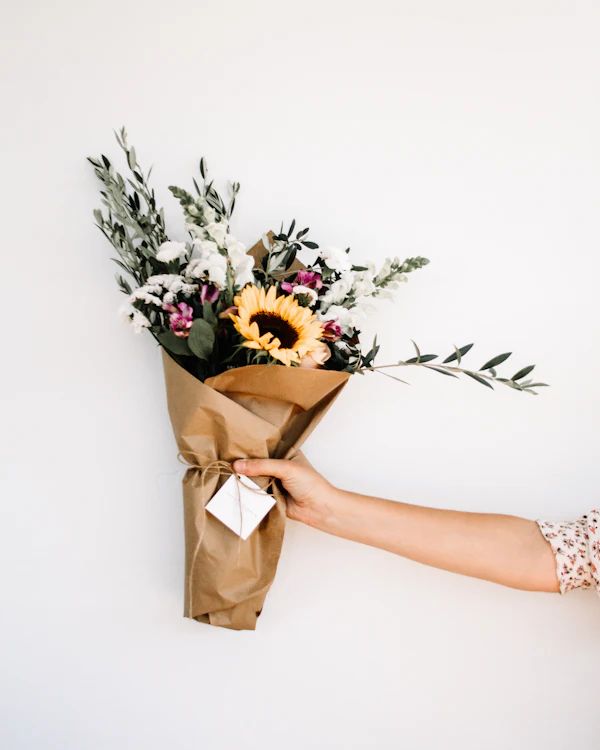 Hand hält einen Strauß mit Sonnenblume in Packpapier
