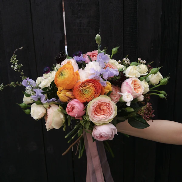 Bunter Strauß aus Ranunkeln und Rosen in der Hand