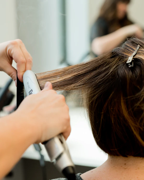 Hände glätten eine Haarsträhne mit dem Glätteisen
